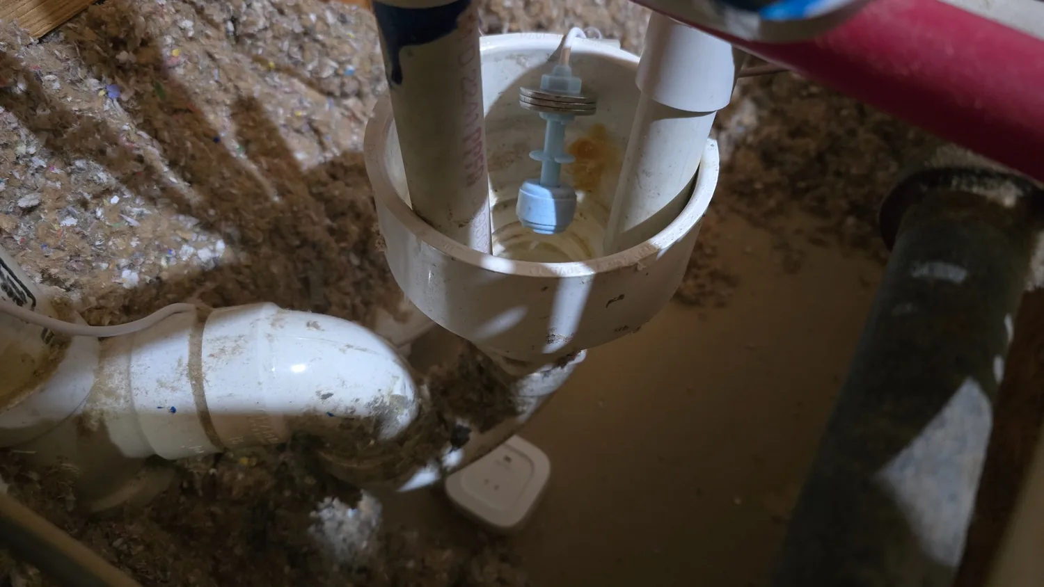 Close-up actual white PVC bowl with blue water level probe and separate leak detection hardware next to attic floor
